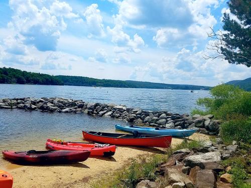 Colorful kayaks on a sandy shore by a calm lake, with rocky formations and a blue sky filled with fluffy clouds.