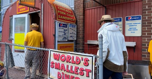 Two people approach a small diner with a sign reading "World's Smallest Diner" in a vibrant, colorful setting.