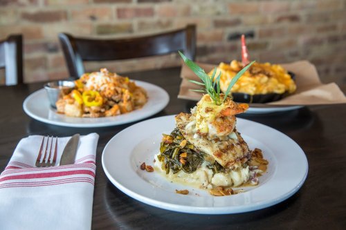 A plate of grilled fish with greens and mashed potatoes, with mac and cheese and another dish in the background.