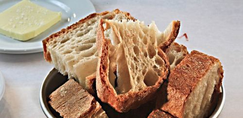 A bowl of assorted bread slices, including crusty and soft pieces, with a pat of butter in the background.
