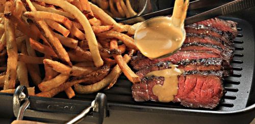 A juicy steak topped with sauce, served alongside a generous portion of crispy French fries.
