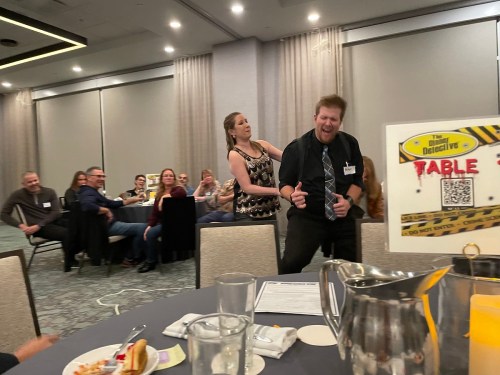 A lively event scene with a woman playfully interacting with a man, while guests enjoy the gathering in the background.