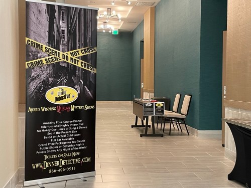 A hallway featuring a banner for a murder mystery show and a table with chairs, promoting an interactive dining experience.