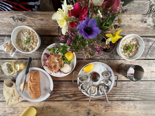 A rustic table set with seafood dishes, a loaf of bread, and a vibrant flower arrangement.