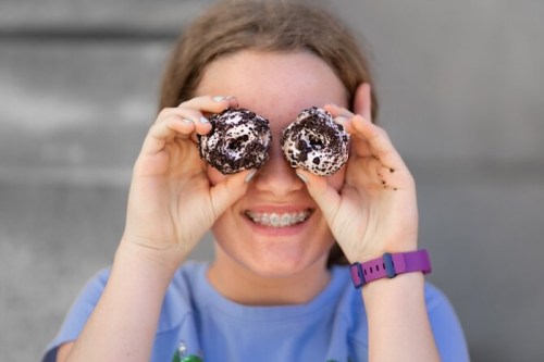 A smiling girl holds two chocolate-covered treats up to her eyes, playfully posing for the camera.