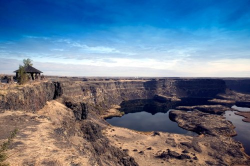A scenic view of a canyon with a calm lake, surrounded by rocky cliffs and a clear blue sky.