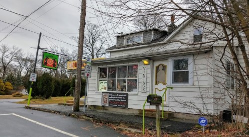 A vintage shop in a white house, with a sign and colorful decorations, set along a quiet road on a cloudy day.