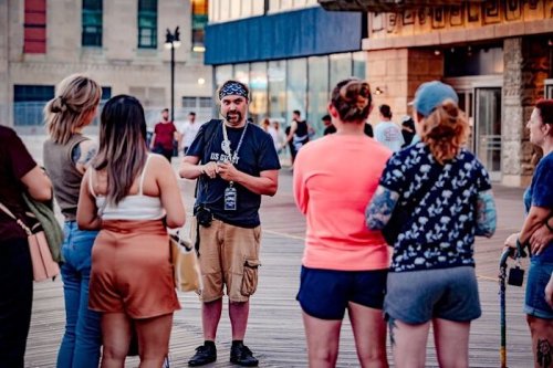 A group of people listens to a man speaking on a boardwalk during an outdoor event.