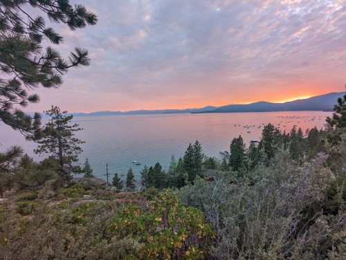 A serene lake view at sunset, with boats on the water and trees framing the scene under a colorful sky.