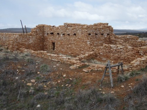 Ruins of a stone structure in a grassy landscape, with cloudy skies in the background.
