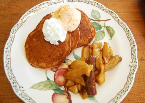A plate of pancakes topped with whipped cream and ice cream, served with a side of caramelized apples.