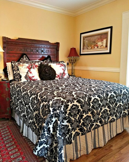 A cozy bedroom featuring a patterned bedspread, wooden headboard, and decorative lamps against a warm yellow wall.