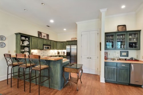A cozy kitchen with green cabinets, a central island with bar stools, and stainless steel appliances.