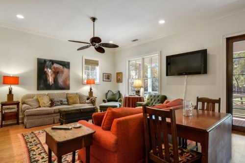 Cozy living room with a mix of seating, a TV, and large windows, featuring warm lighting and a horse painting.