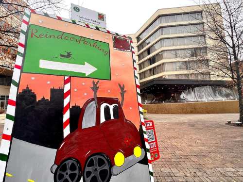 A festive sign for "Reindeer Parking" featuring a cartoon car with raised hands, set against a wintery backdrop.