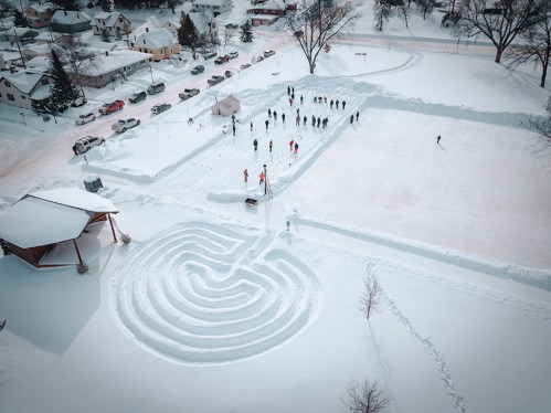 Aerial view of a snowy park with a maze, ice rink, and people enjoying winter activities.
