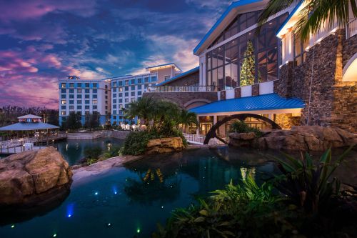 A scenic view of a resort at dusk, featuring a pool, lush landscaping, and a modern building with large windows.