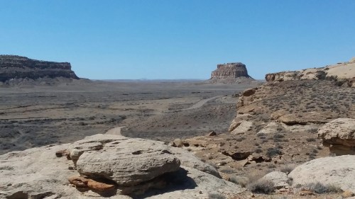 A vast desert landscape with rocky formations and a clear blue sky in the background.