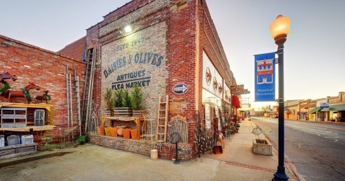 A brick building with "Antiques Flea Market" signage, featuring vintage decor and a quiet street scene.