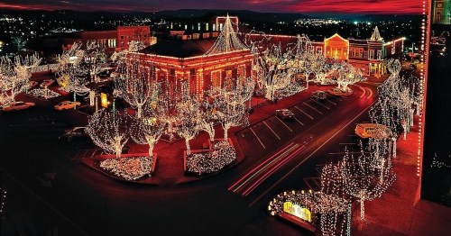 Aerial view of a festive town square adorned with colorful holiday lights and decorated trees at dusk.