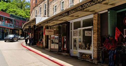 A charming street scene featuring shops and an eatery, with people walking and a car parked along the curb.