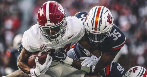 A football player in a white jersey is tackled by an opponent in an orange and blue jersey during a game.