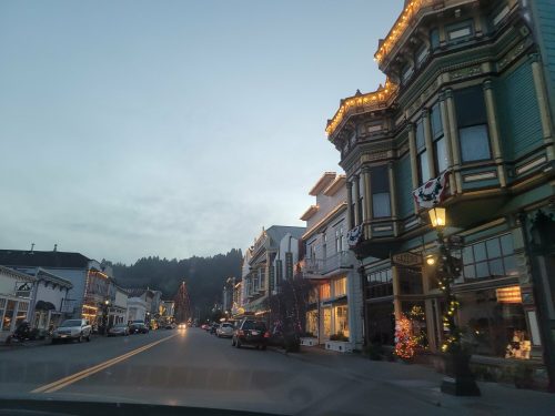 A charming street lined with historic buildings, decorated for the holidays, under a twilight sky.