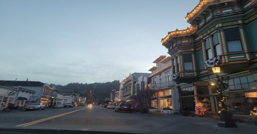 A charming street lined with historic buildings, decorated with lights, under a twilight sky.