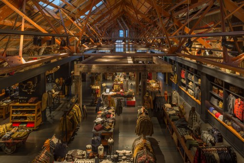 A spacious retail store with wooden beams, showcasing various clothing items arranged on tables and racks.