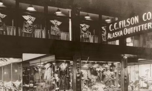 Historic storefront of C.C. Filson Co. featuring outdoor clothing and gear, with displays in windows and on the balcony.