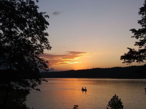 A serene sunset over a lake, with two people in a small boat silhouetted against the colorful sky.