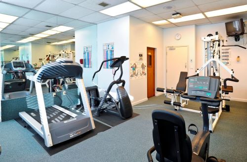 A bright gym with various exercise equipment, including treadmills, an elliptical, and weight machines.