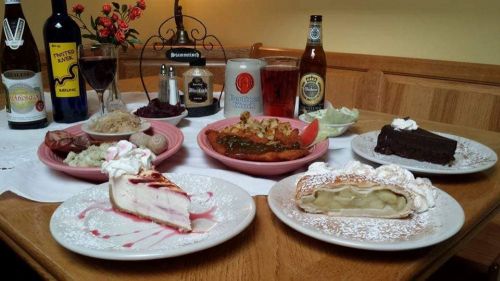 A table set with various dishes, including meats, desserts, and drinks, showcasing a hearty meal spread.