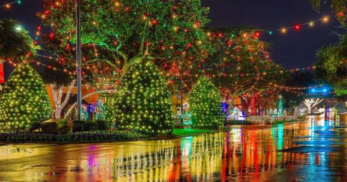 A festive street adorned with colorful Christmas lights reflecting on wet pavement at night.