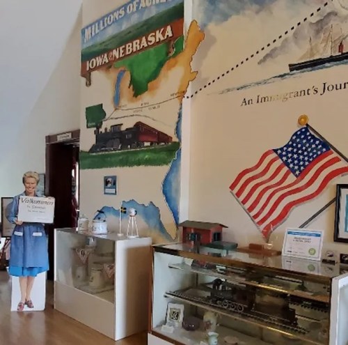 Interior of a museum featuring a mural of Iowa and Nebraska, with displays and a cutout of a woman holding a sign.