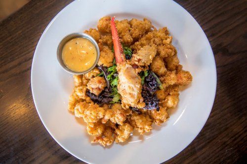 A plate of crispy fried seafood with a dipping sauce and greens, featuring a prominent lobster claw on top.
