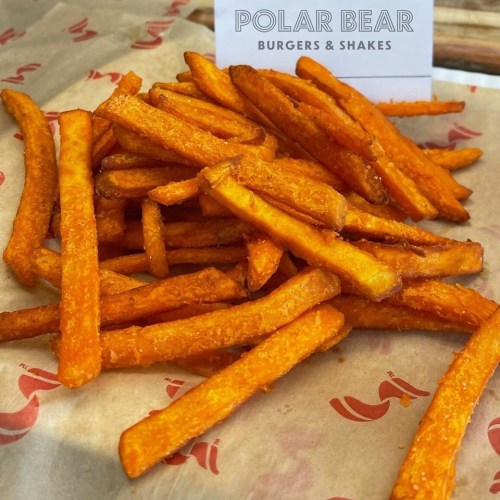 A pile of golden-brown sweet potato fries on parchment paper, with a sign for "Polar Bear Burgers & Shakes" in the background.