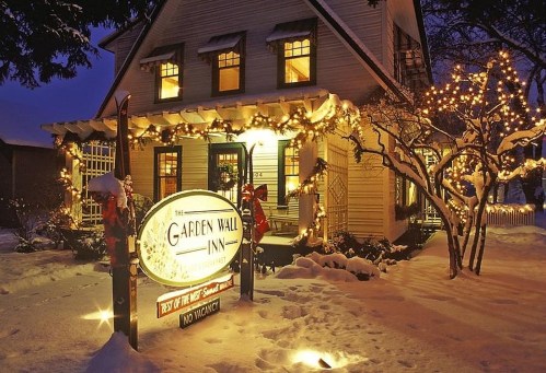 A cozy inn decorated with holiday lights, surrounded by snow, creating a warm winter atmosphere at dusk.