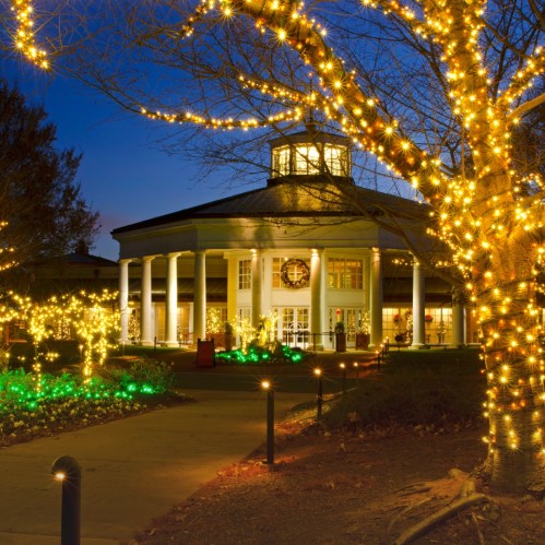 A beautifully lit building surrounded by festive lights and greenery at dusk.