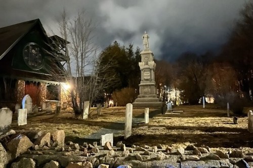 A dimly lit graveyard at night, featuring a tall monument and scattered gravestones under a cloudy sky.