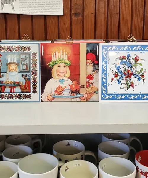 Three decorative plates featuring festive illustrations, displayed on a shelf above various mugs.