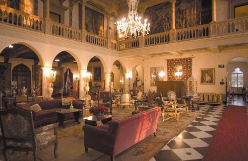Luxurious interior of a grand room with ornate decor, chandeliers, and elegant furniture, featuring a checkered floor.
