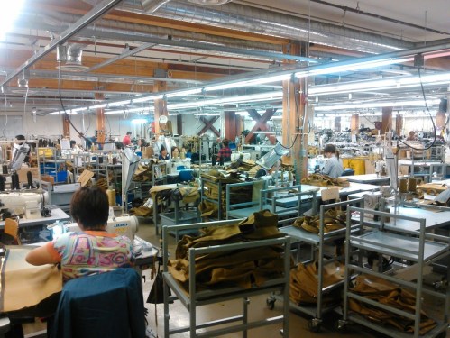 A busy manufacturing workshop with workers at sewing machines and tables filled with fabric and materials.