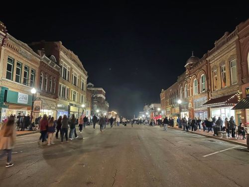 A bustling street at night, lined with historic buildings and crowds of people enjoying the atmosphere.