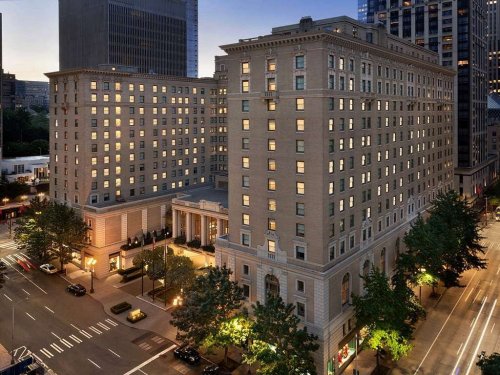 Historic hotel building illuminated at night, surrounded by trees and city streets.