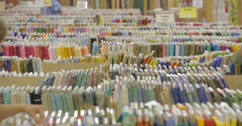 A vibrant display of colorful fabric bolts arranged neatly in a craft store, with labels visible on each bolt.