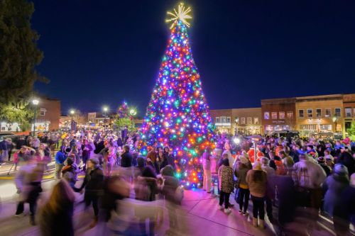 A vibrant Christmas tree adorned with colorful lights, surrounded by a crowd celebrating in a festive evening atmosphere.