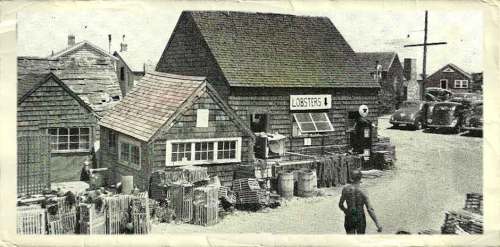 Black and white photo of a seaside lobster shop with wooden buildings and a person walking nearby.