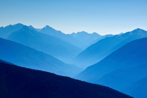 A serene landscape of layered blue mountains under a clear sky, with valleys and ridges creating a tranquil scene.