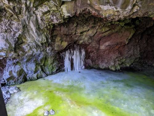 A rocky cave with greenish water and icicles hanging from the ceiling, creating a serene, natural scene.